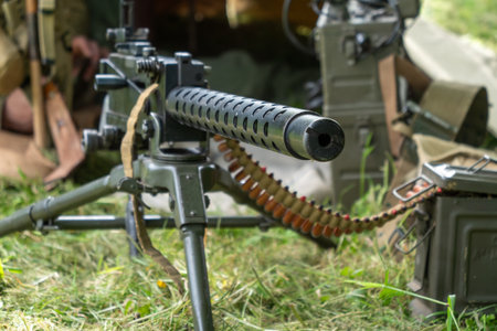 A black machine gun with a long barrel is on a grassy field. The gun is surrounded by a lot of...