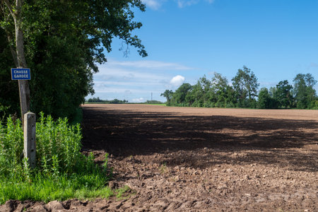 A field of dirt with a sign. The sky is blue and there are trees in the backgroundの写真素材