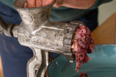 A person is using a meat grinder to grind meat. The meat is being ground into small piecesの写真素材