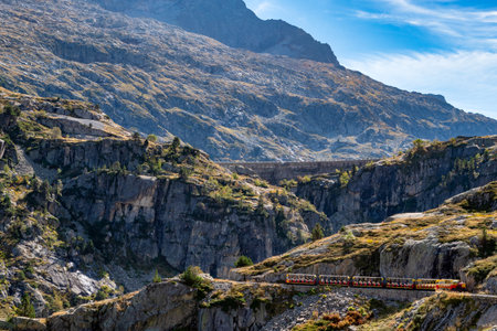 A train is traveling down a mountain track. The train is surrounded by mountains and the landscape is rocky and barren.の写真素材