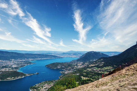 A beautiful view of a lake of Annecy with mountains in the background. The sky is mostly clear with a few clouds scattered aroundの写真素材
