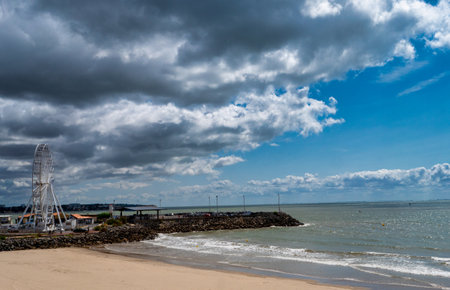 Beach with a large Ferris wheel in the background. The sky is cloudy and the water is calm