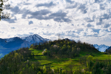 Mountain range with a cloudy sky and a small house in the middle. The house is surrounded by trees and the mountains are covered in snow. The scene is peaceful and sereneの写真素材