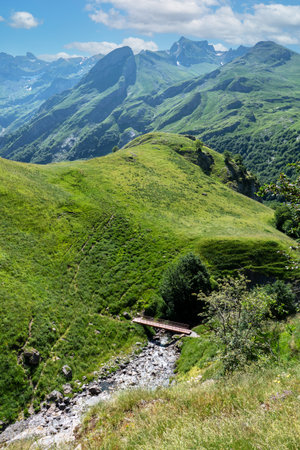 Mountain range with a green hillside and a bridge over a river. The bridge is wooden and is located in the middle of the mountain rangeの写真素材