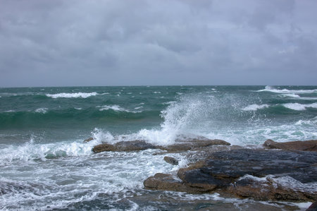 The ocean is rough and the waves are crashing against the rocks. The sky is cloudy and the water is a deep blue colorの写真素材