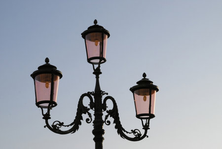 Three street lamps with pink lights are on a pole. The lamps are on a clear day. The sky is blue and the sun is shiningの写真素材
