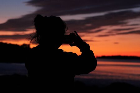Young girl photographing an ocean sunrise on her phone