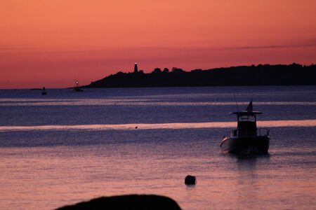 Boat on ocean at sunrise, lighthouse in backgroundの写真素材