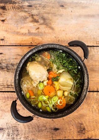 Delicious dinner or lunch, chicken soup with vegetables and noodles served in a black bowl on the background of a wooden table.の写真素材
