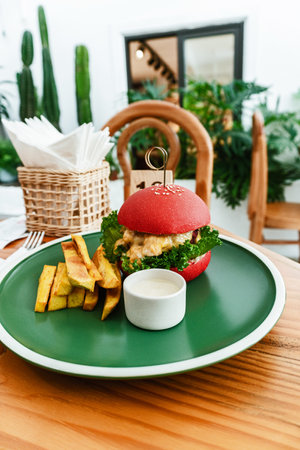 Vegan burger, in a red bun, dish with chips, on a green plate, on a wooden table, healthy vegetarian food, in an aesthetic bright approach.の写真素材