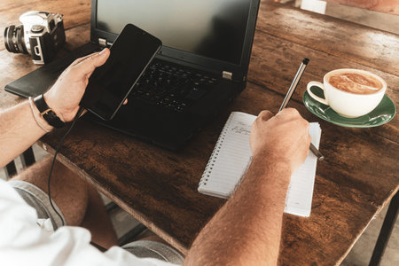 Cropped image of young man working on laptop and drinking coffee in cafe