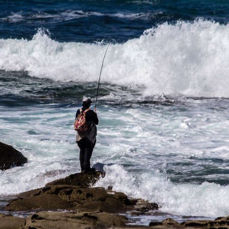 fisherman on a rock, in the middle of the wavesの写真素材