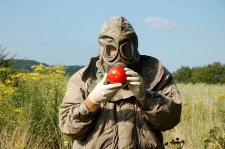 Man in gas mask holding contaminated tomatoの写真素材