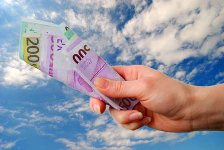 Hand with euro bank notes against blue sky