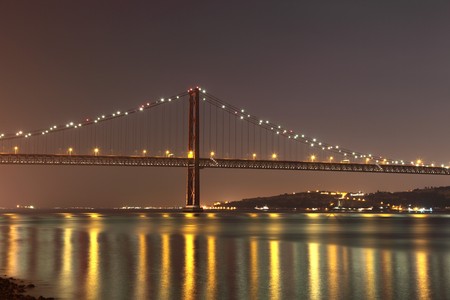 The 25 de Abril Bridge - suspension bridge over the river Tagus illuminated at night. Lisbon,...