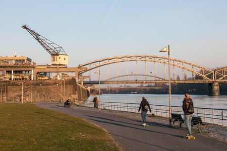 FRANKFURT, GERMANY - MAR 14: Young people skateboarding at the Main river bank in Frankfurt. Old steel railway bridge and old port crane in the background. March 14, 2016 in Frankfurt, Germanyのeditorial素材