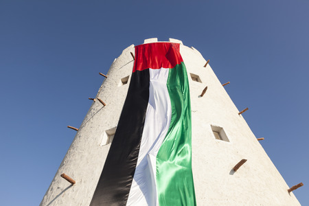 Old tower in Abu Dhabi decorated with huge UAE flag for the celebration of 45th National Day の写真素材