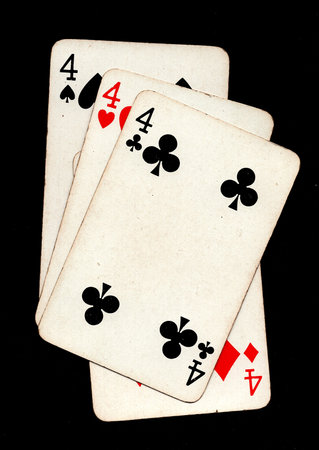 A hand of four vintage playing cards of the same value isolated on a black background.
