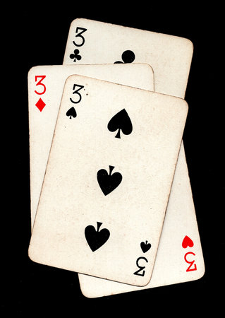 A hand of four vintage playing cards of the same value isolated on a black background.