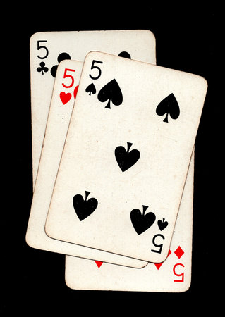 A hand of four vintage playing cards of the same value isolated on a black background.