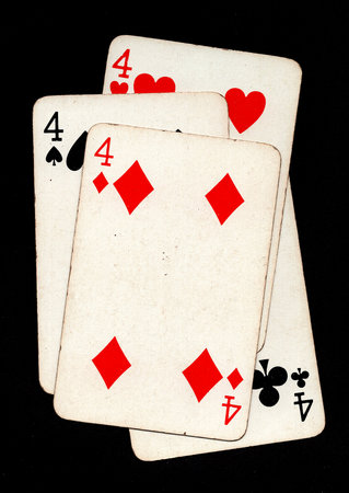 A hand of four vintage playing cards of the same value isolated on a black background.の写真素材
