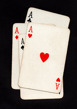 A hand of four vintage playing cards of the same value isolated on a black background.