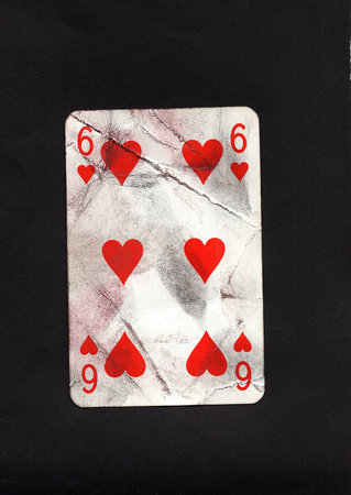 A grubby old playing card in the suit of hearts on a black background.