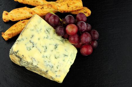 Blue veined strong English Stilton cheese wedge and red grapes on a stone slate backgroundの写真素材
