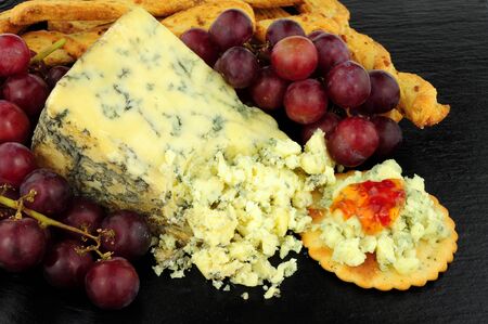 Blue veined strong English Stilton cheese wedge and red grapes on a stone slate backgroundの写真素材