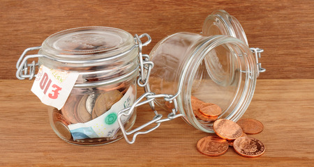 Glass jars filled with cash savings one empty and one full on a wood background