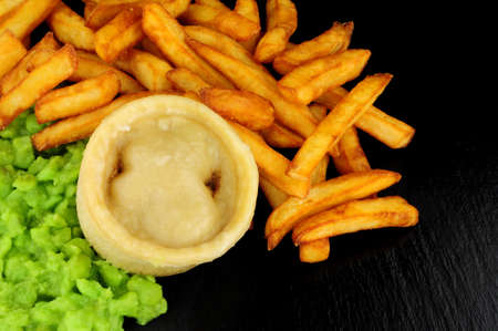 Steak and kidney pudding and chips meal with mushy peas meal on a slate backgroundの写真素材