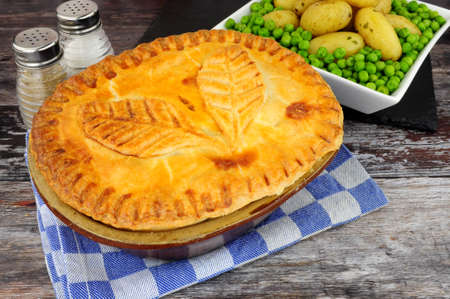 Beef steak pie in a glazed shortcrust pastry case with a pastry leaf decoration served with new...