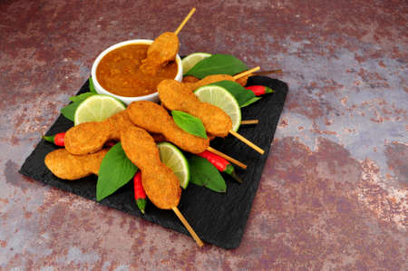Chicken satay skewers with peanut dipping sauce and lime fruit on a slate serving boardの写真素材