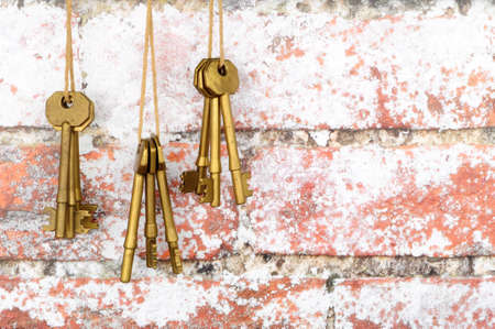 Old brass metal door keys hanging from string against a rustic brick wall texture background