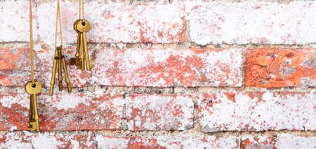 Old brass metal door keys hanging from string against a rustic brick wall texture background