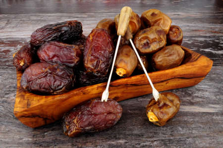 Group of ripe soft and sticky medjool and zamli dates in an olive wood serving dish