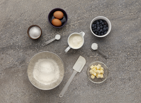 Blueberry muffin ingredient mixture, shot on a stone work surface, inluding eggs, flour, butter and sugar.の写真素材