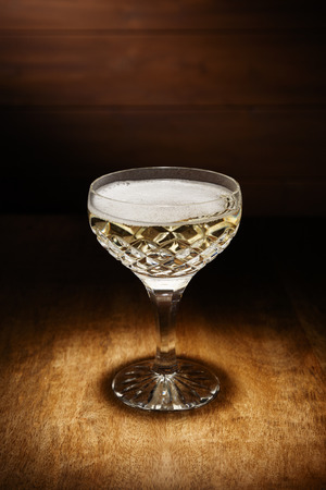 Spotlight on a crystal glass of Champagne, shot on a antique wooden table top.の写真素材