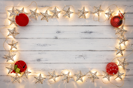 A string of golden star christmas lights, and red baubles, on a destressed woodern background, creating a border around an empty space for copyの写真素材