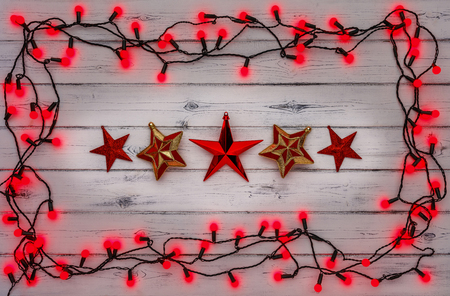 A string of red holly berry christmas lights, and a row of red stars, on a destressed woodern backgroundの写真素材