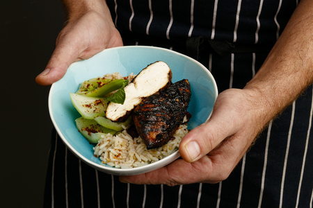 Close up of a chefs hands presenting a bowl of Jerk chicken with rice and vegetablesの写真素材