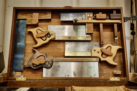 Traditional woodworking hand saws and carpentry tools in a cabinetの写真素材