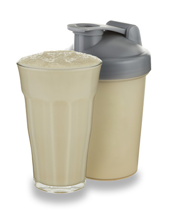 A glass of vanilla milkshake and shaker on a white background with a drop shadowの写真素材