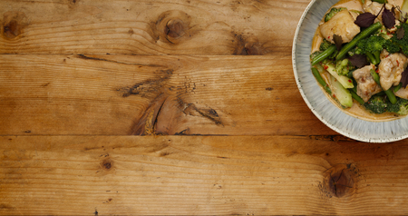 A bowl of succulent Thai Red Chicken Curry shot a wooden background in a banner format with space for copyの写真素材