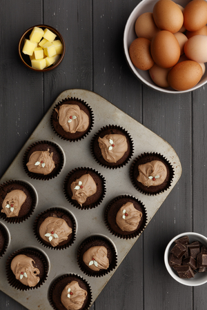 Fairy cakes in baking tray with  ingredients, on a distressed grey wooden background, shot from aboveの写真素材