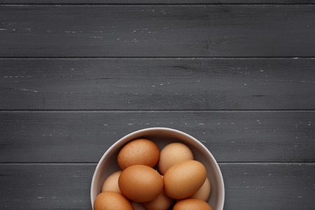 A bowl of fresh eggs on a distressed wooden background, shot from above, with space for copyの写真素材