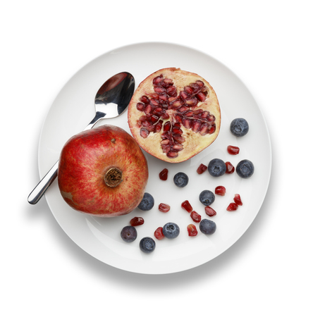 blueberries and pomegranate with a silver spoon on white plate on a white backgroundの写真素材