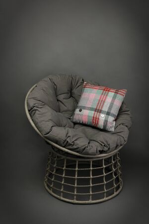 side on view of a wicker chair and soft seating cushion and a colourful cushion on grey backgroundの写真素材