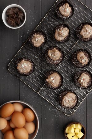 Fairy cakes on a cooling tray with a dusting of icing sugar and   ingredients, on a distressed grey wooden background, shot from aboveの写真素材
