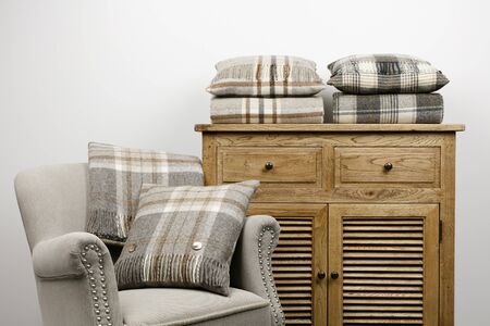 Chair and side cabinet with natural coloured checked cushions and throws, against  a white background.の写真素材